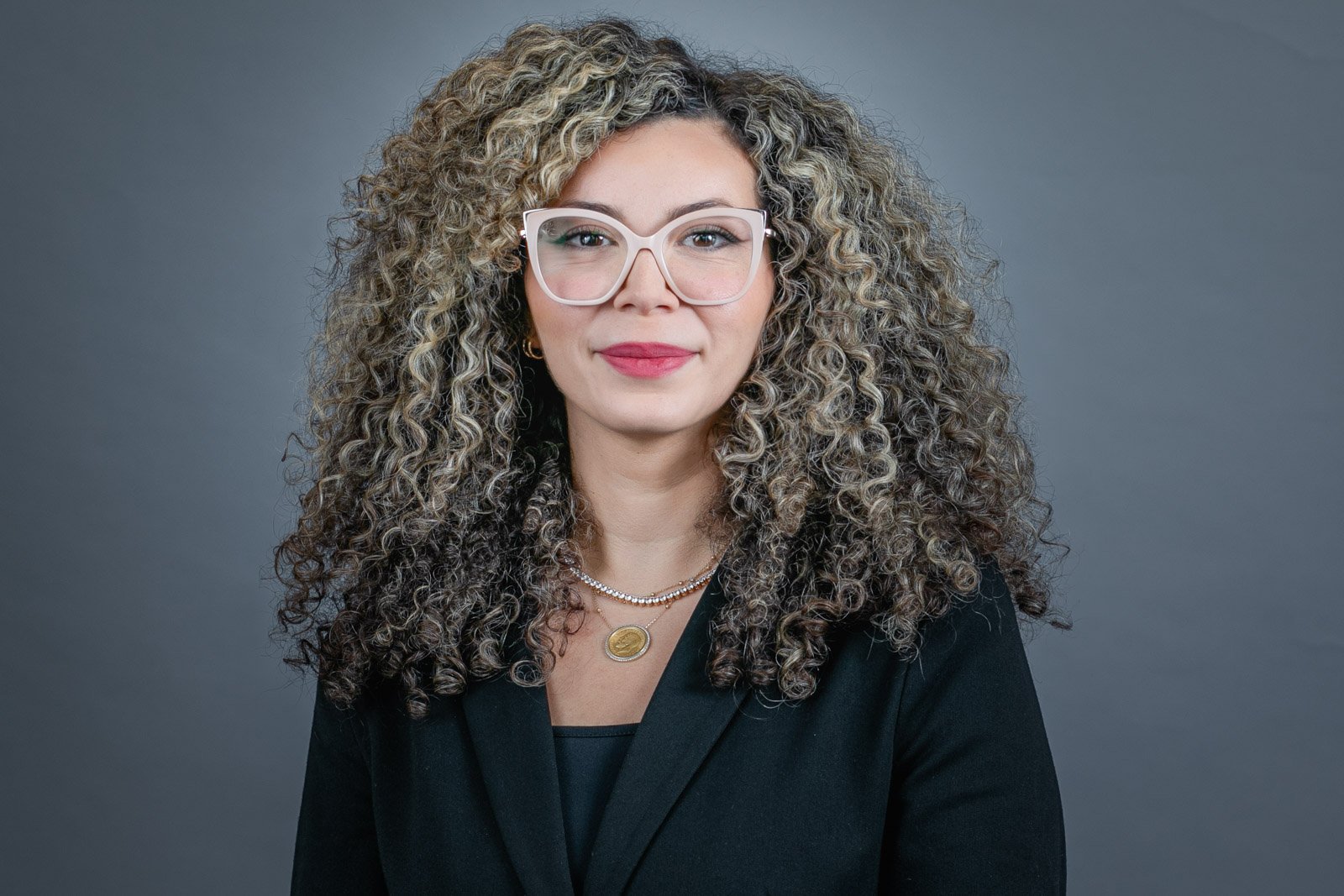 Professional headshot of a female lawyer, professionally dressed. Photographed in Livonia, Michigan, by Hugh Anderson Photography of Bloomfield Hills. Female, lots of curly hair, professional dress, studio headshot.