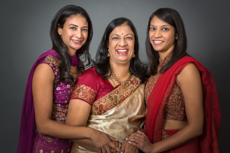 Mothers day family portrait. Photograph of an Indian lady, flanked by her to grown up daughters, in full Indian dress. A studio portrait with expert lighting and a dark backdrop.