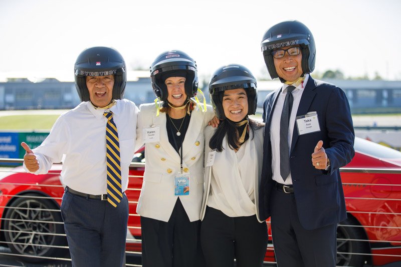 Corporate guests in helmets pose with race car at M1 Concourse in Pontiac, MI