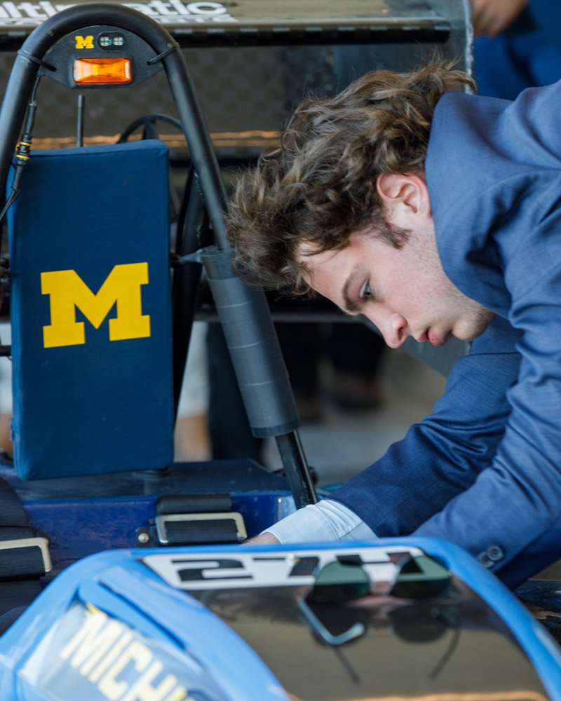 Engineering Student Examines Branded Race Car at M1 Concourse, Michigan Corporate event photography of engineering student inspecting race car at University of Michigan–branded M1 Concourse display
