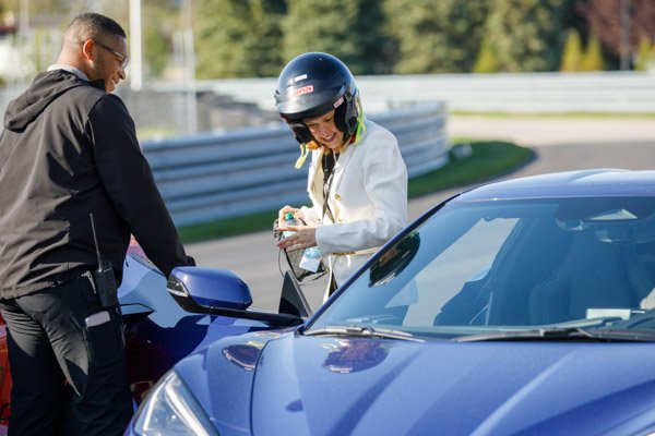 SAE International event participant wearing a helmet prepares to enter a blue Corvette at M1 Concourse in Pontiac, Michigan