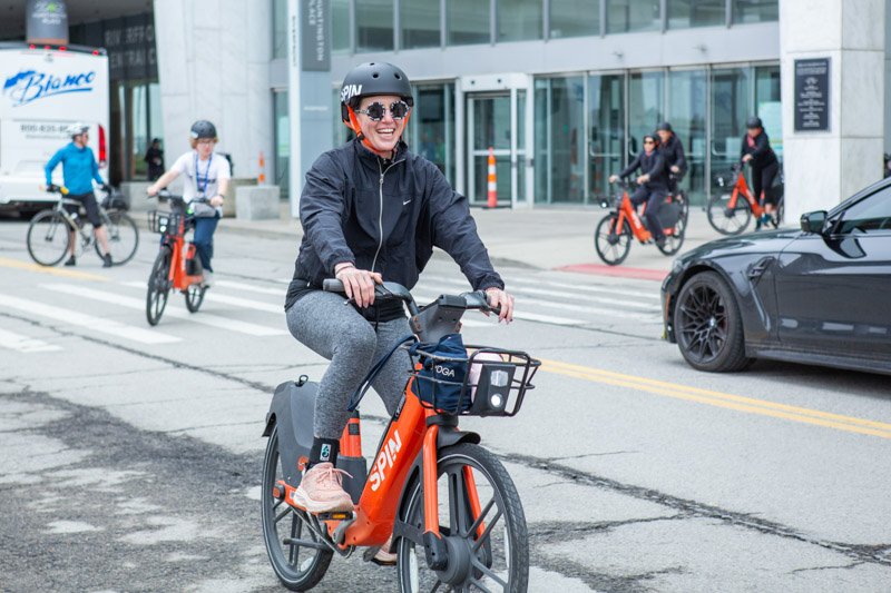 Conference attendee riding a bicycle through downtown Detroit during an organized networking bike tour at a multi-day conference.