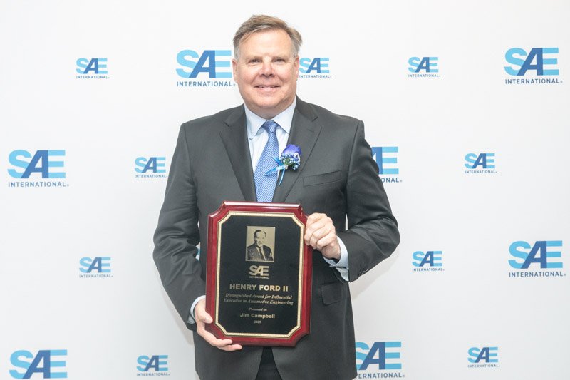 SAE award recipient photographed in front of a branded step and repeat backdrop